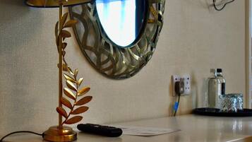 A desk with a lamp, a remote control, a mirror, a water bottle, and a power outlet.