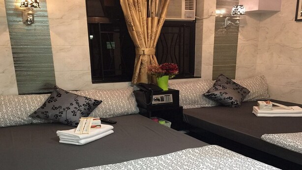 A hotel room with two beds, each with patterned bedding, a vase with flowers, and a small table with a remote control. - Rich Hostel (Kowloon)