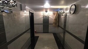 A narrow, tiled hallway with a central stripe pattern, a door on the left, and a clock on the right wall. - Rich Hostel (Kowloon)
