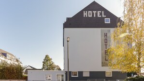 Un moderno edificio de hotel con un cartel grande que dice 'HOTEL' en el techo, un ventanal lateral y un estacionamiento cercado.