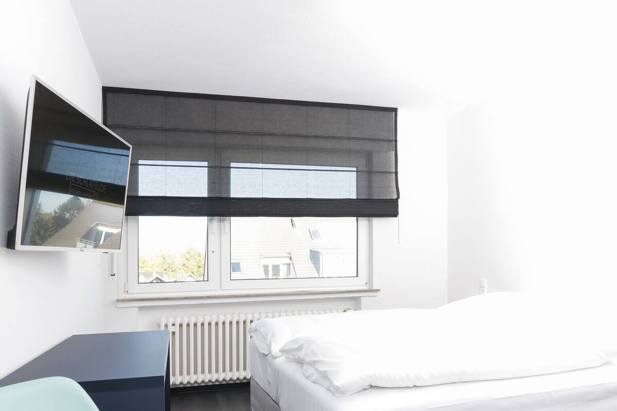 Un dormitorio moderno con cama, escritorio, silla, ventana con vistas y televisor montado.