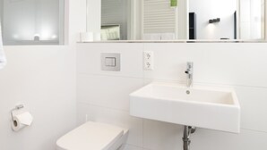 Un baño moderno con un lavamanos blanco, un inodoro y un espejo.