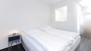 Habitación de hotel minimalista con una cama individual, una mesita de noche con lámpara y un amplio ventanal que proporciona luz natural.