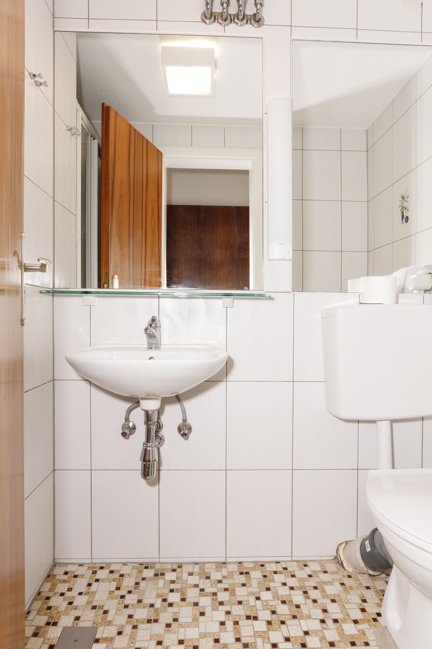Ein Badezimmer mit einem weißen Waschbecken, einem Glasspiegel und einer weißen Toilette.