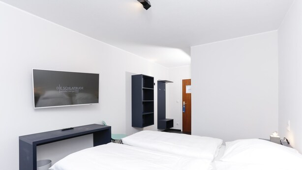 Una habitación de hotel moderna con una cama, un televisor montado en la pared, un escritorio y estanterías empotradas.