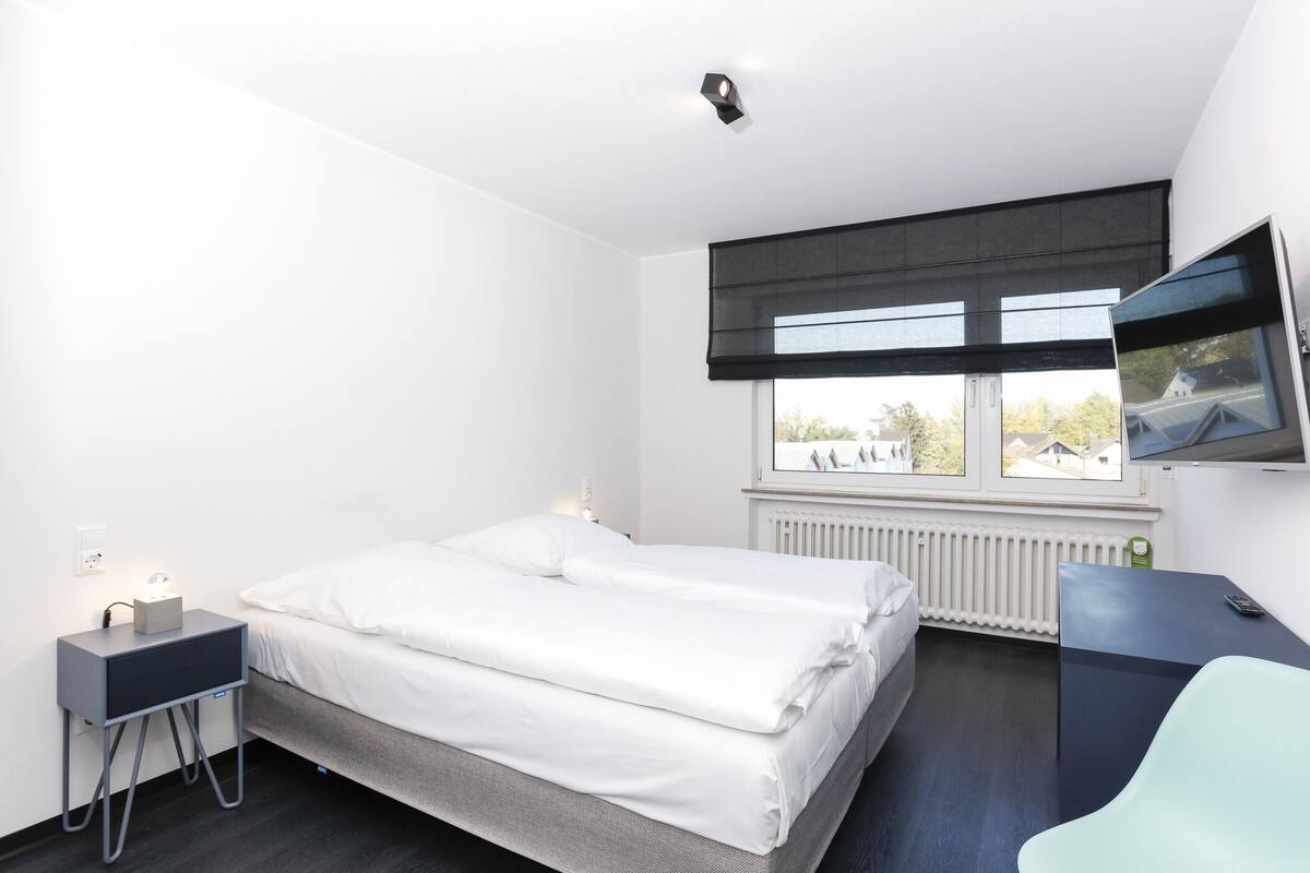 Una habitación de hotel moderna con cama, mesita de noche y televisor montado en la pared.