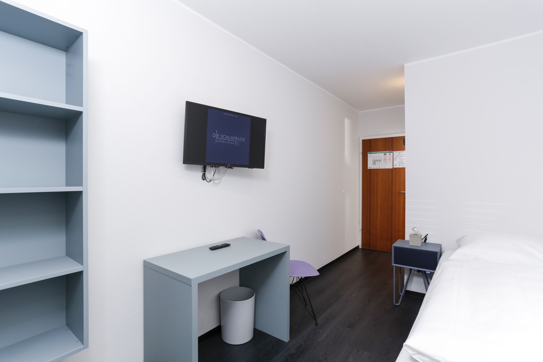 Quarto de hotel moderno com uma cama, uma escrivaninha, uma cadeira, uma televisão e um guarda-roupa.