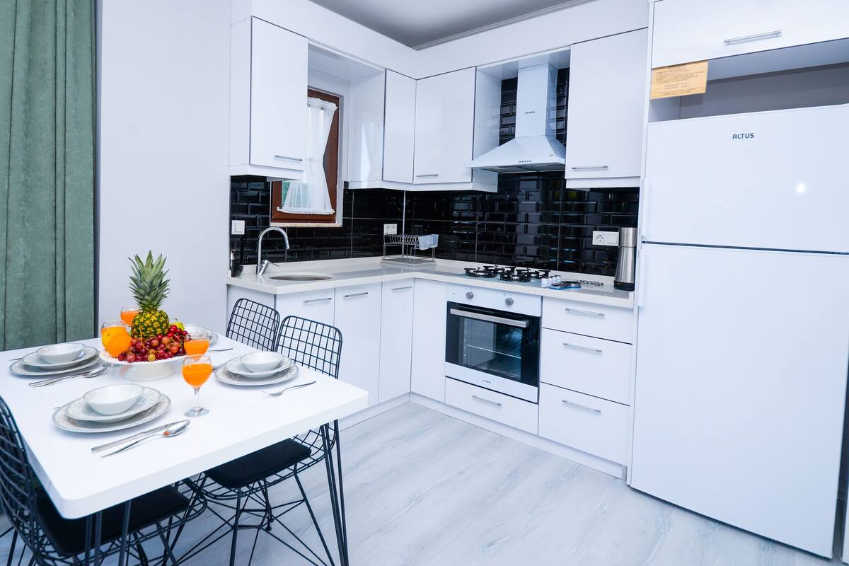 A modern kitchen with white cabinetry, a black backsplash, and a white refrigerator.