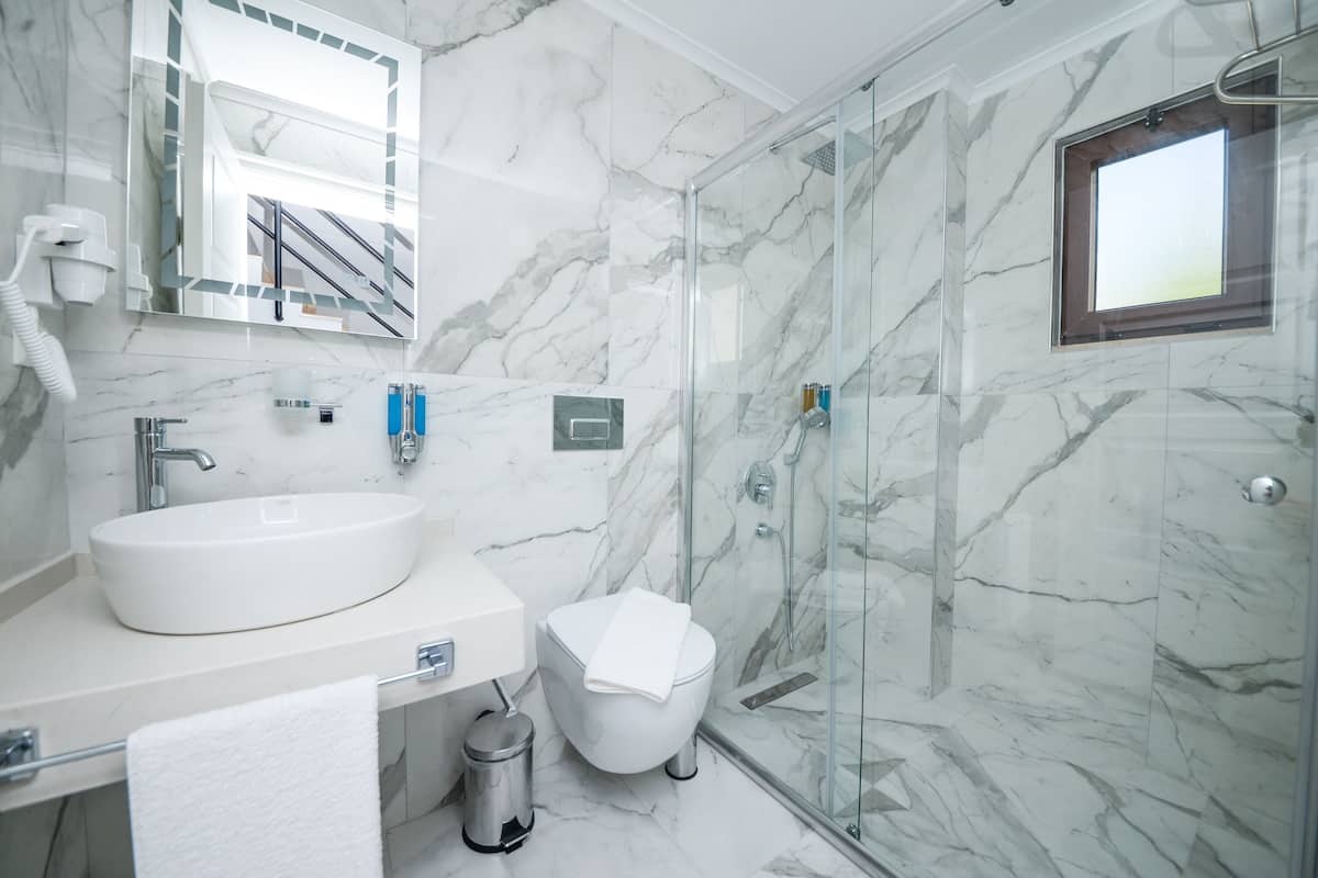 A modern bathroom with a marble sink, a glass shower enclosure, and a toilet.