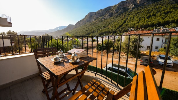 Un balcón con una mesa y sillas de madera, con vistas a un paisaje montañoso y una zona residencial.