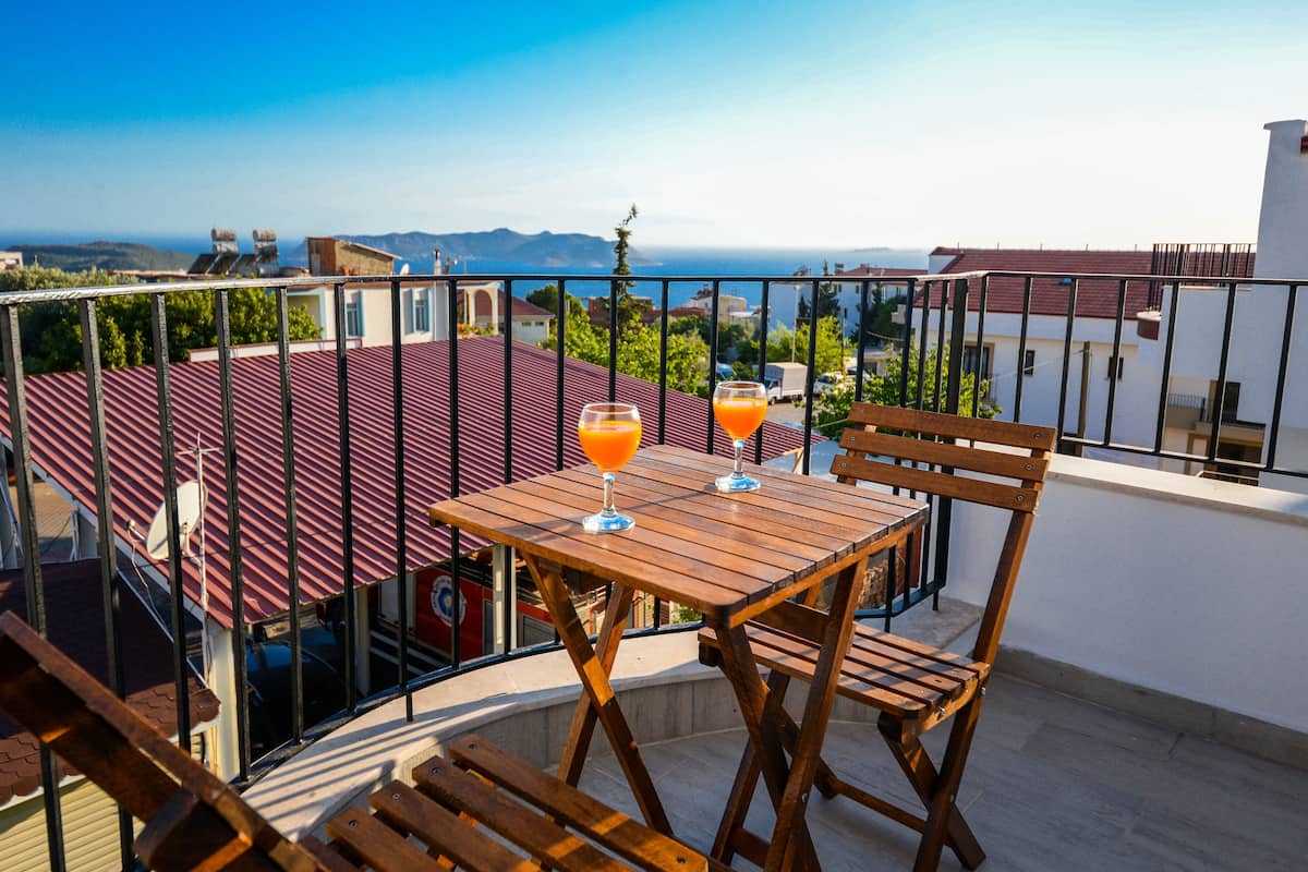 A balcony with a wooden table and chairs, two glasses of orange juice, and a view of the sea and buildings.