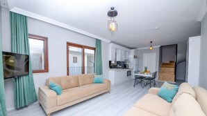 Una sala de estar moderna con un sofá color beige, una mesa de comedor con sillas, una zona de cocina y una escalera.