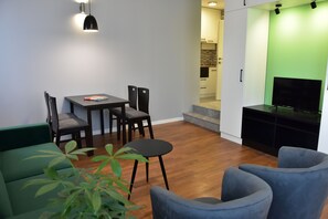 A modern living room with a dining table, chairs, a sofa, a TV stand, and a staircase leading to an upper level. - Osten Art Hotel (Skopje)