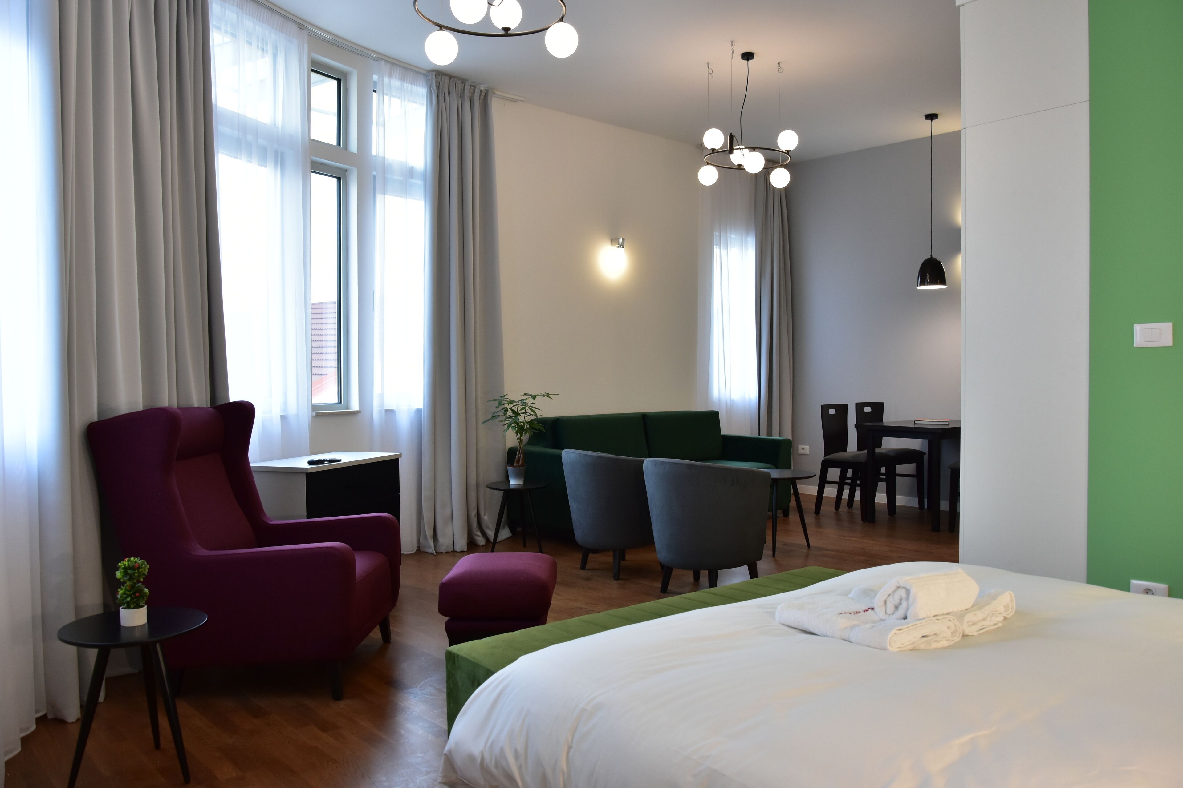 A hotel room with a bed, a desk, a chair, a sofa, and a dining area.