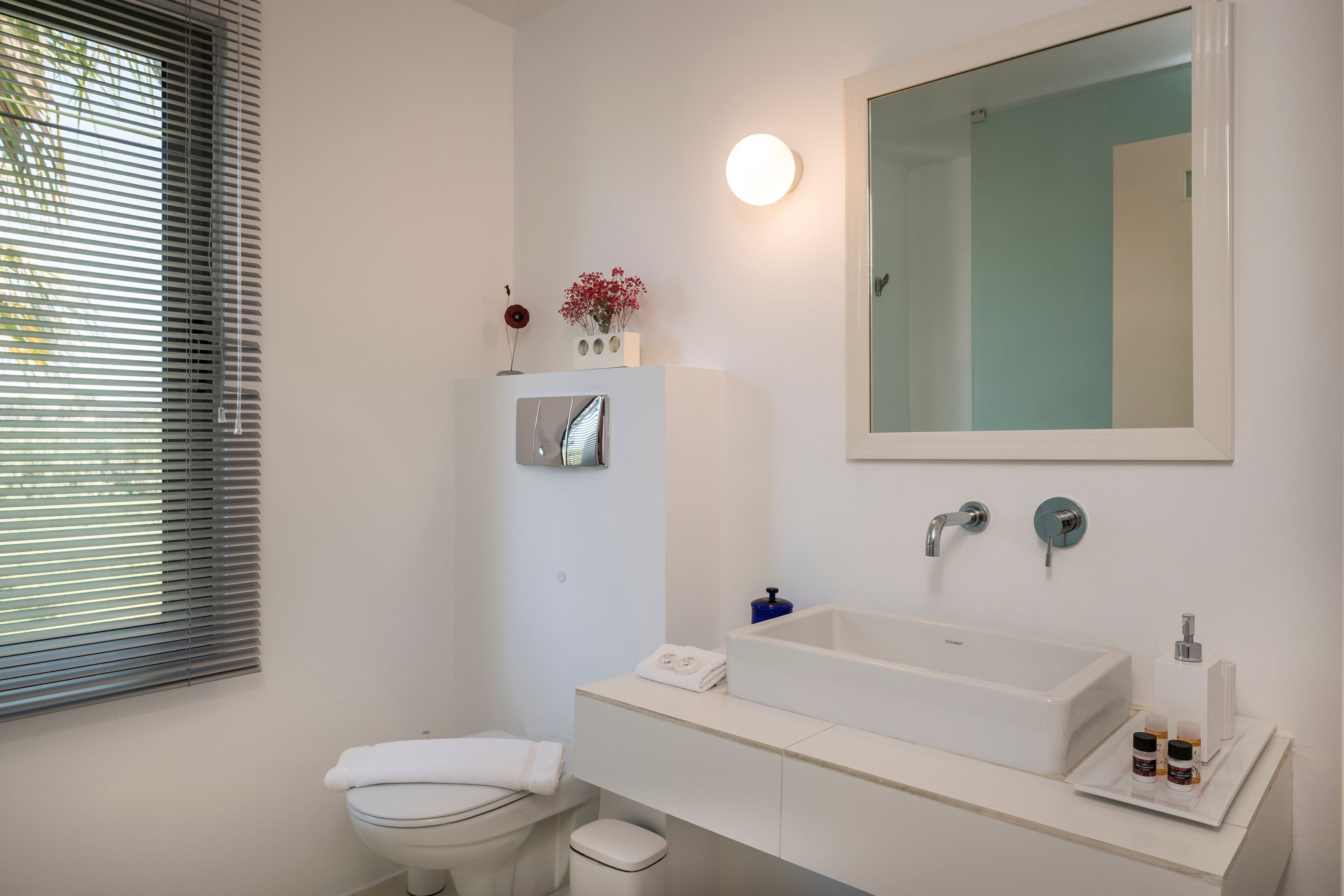 A modern bathroom with a white sink, mirror, and toilet.