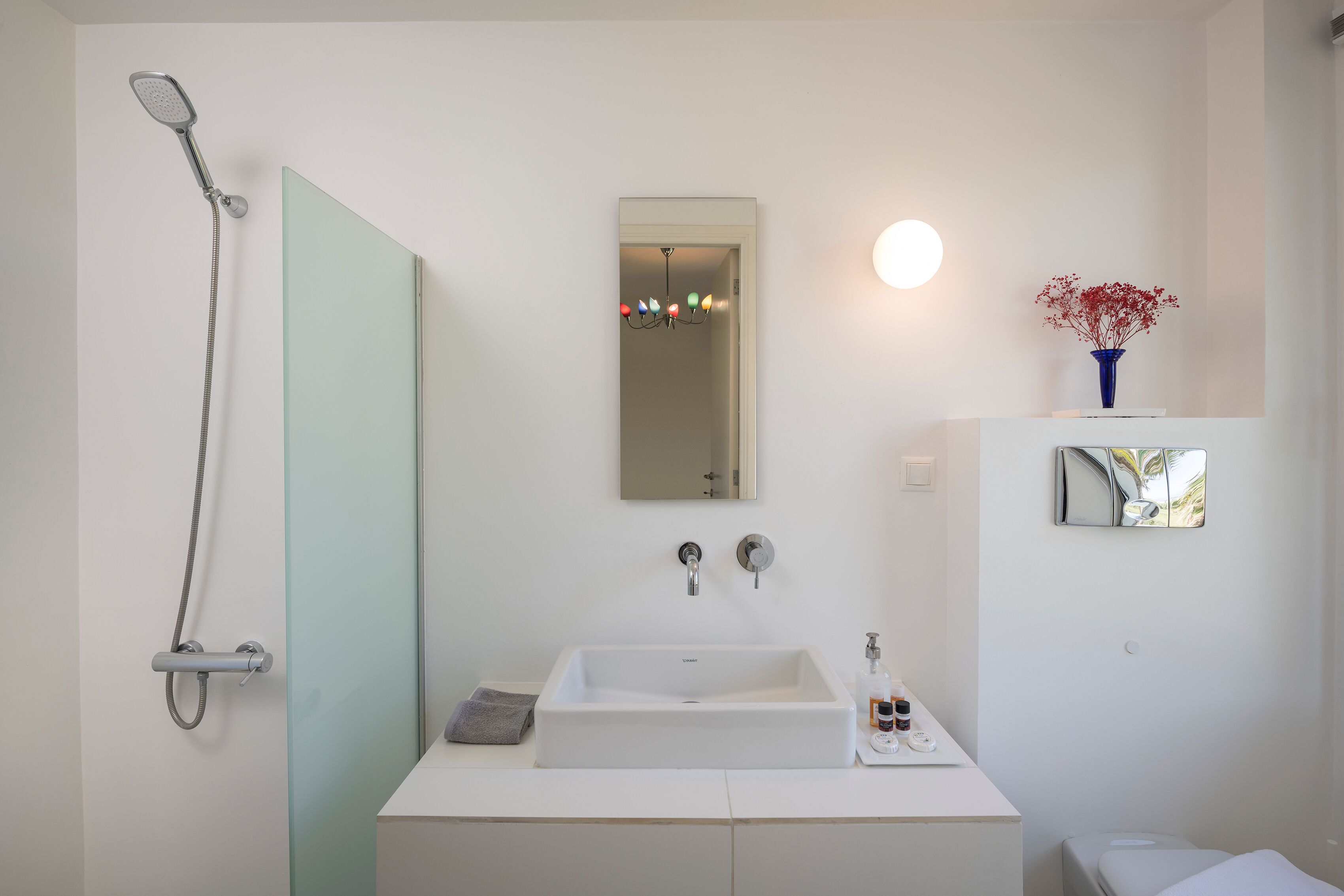 Ein modernes Badezimmer mit Dusche, Waschbecken, Spiegel und einer Vase mit Blumen.