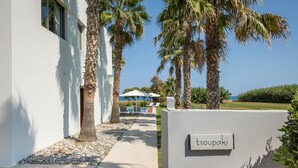 A pathway leading to a pool area with palm trees and a sign reading "tsoupaki".