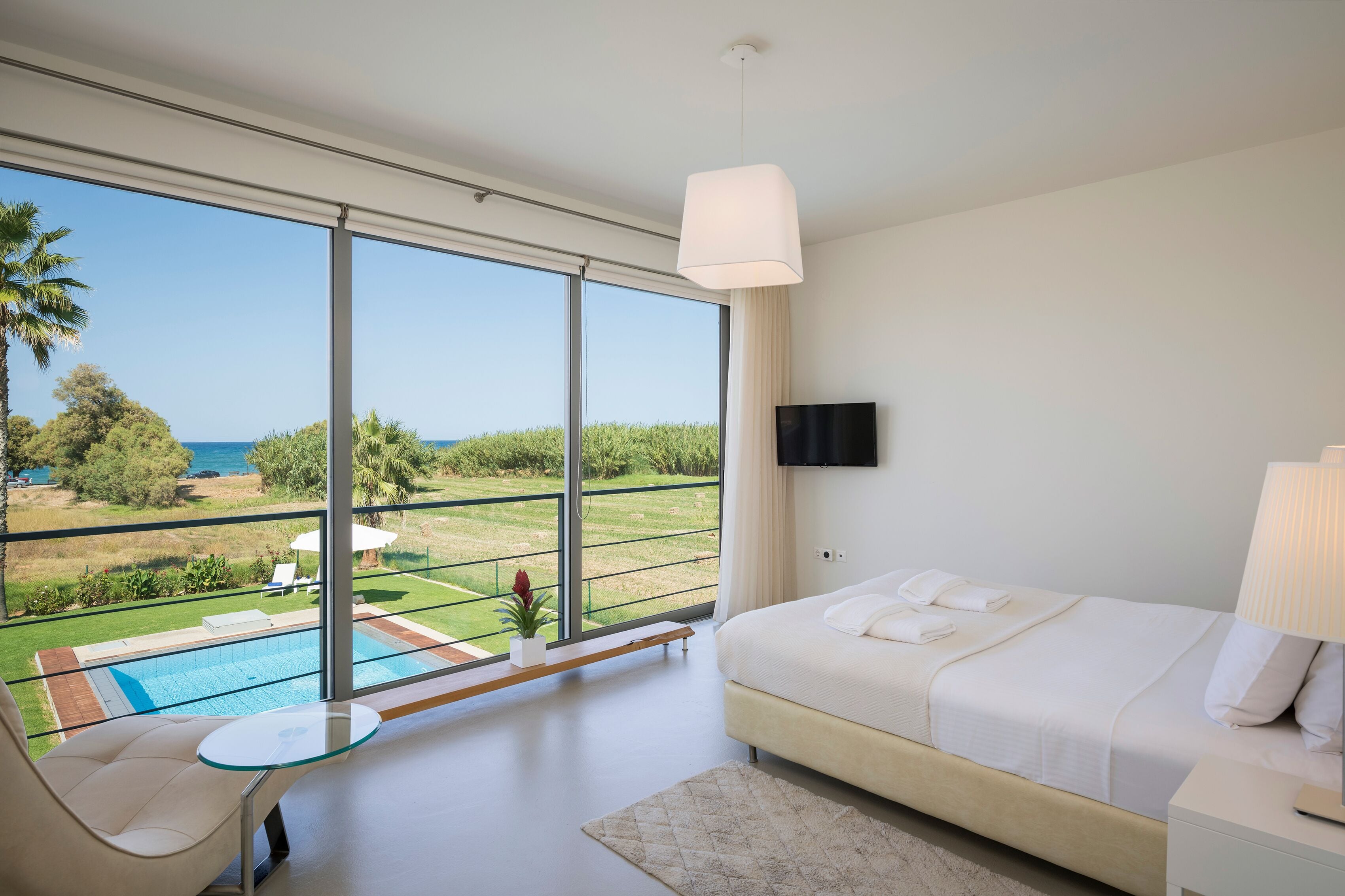 Una habitación de hotel moderna con un balcón grande, una cama, un televisor y vistas a la piscina.