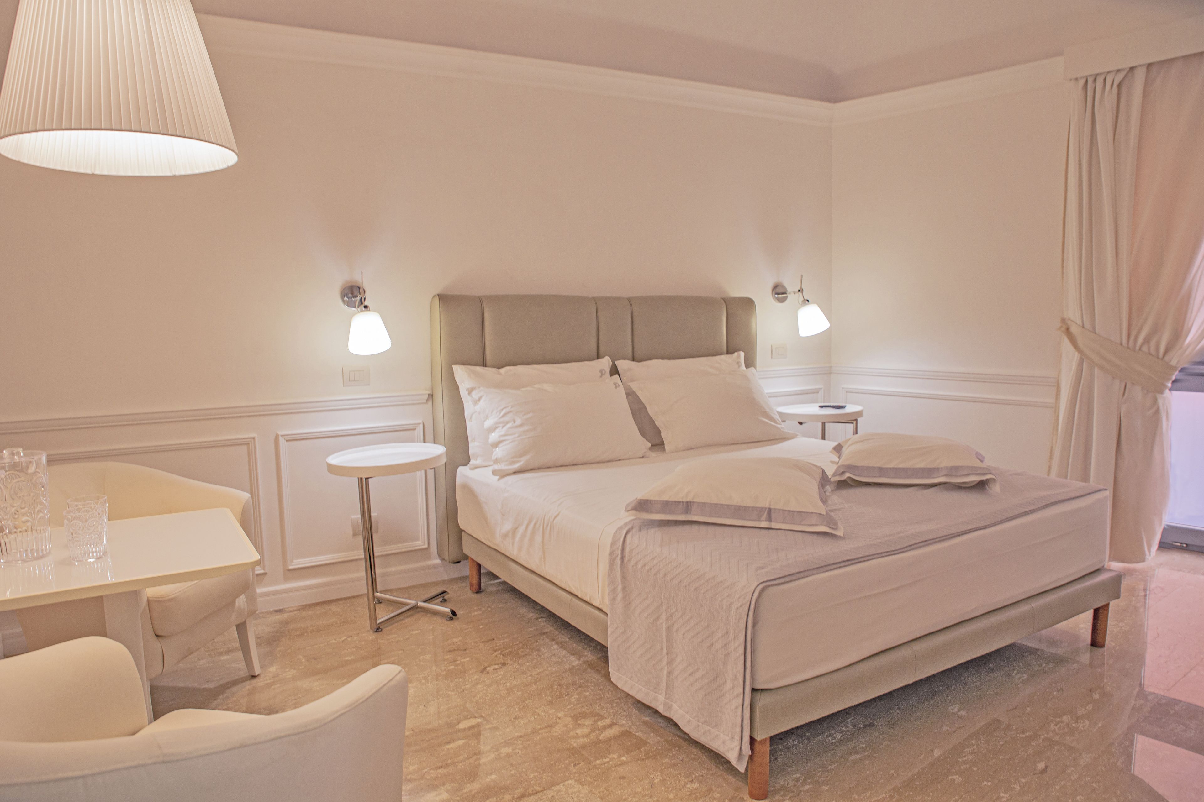 A neatly arranged bedroom with a bed, bedside tables, a small round table, and a chair.