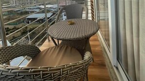 Een balkon met rieten meubilair en uitzicht op een stadslandschap en bergen.
