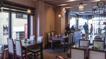 A restaurant with wooden tables and chairs, hanging pendant lights, and a large window with a Coca-Cola sign.