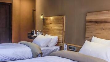 A hotel room with two beds, a wooden headboard, a nightstand with a lamp, and a wall-mounted electrical outlet.