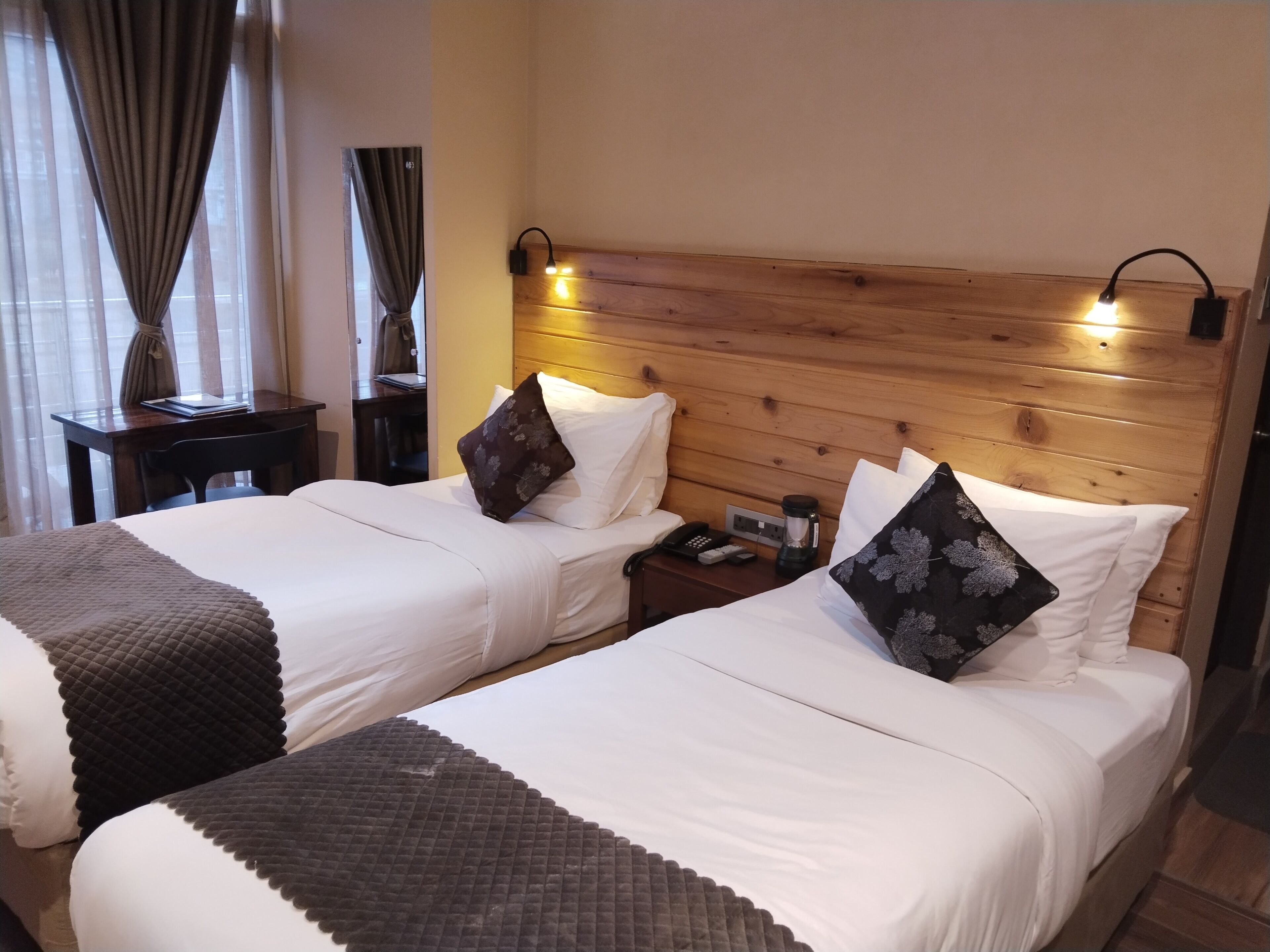 A hotel room with two beds, wooden headboard, bedside tables with lamps, a phone, and a coffee maker.