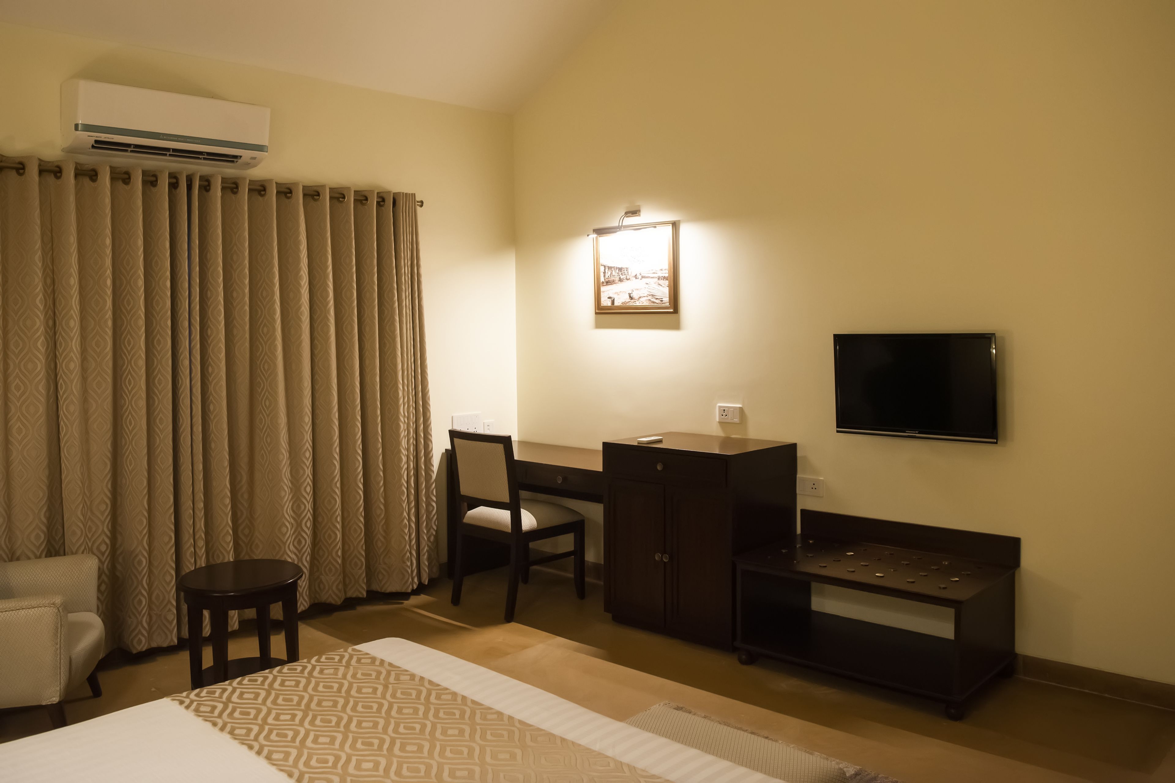 Una habitación de hotel con cama, escritorio, silla, televisión y aire acondicionado.