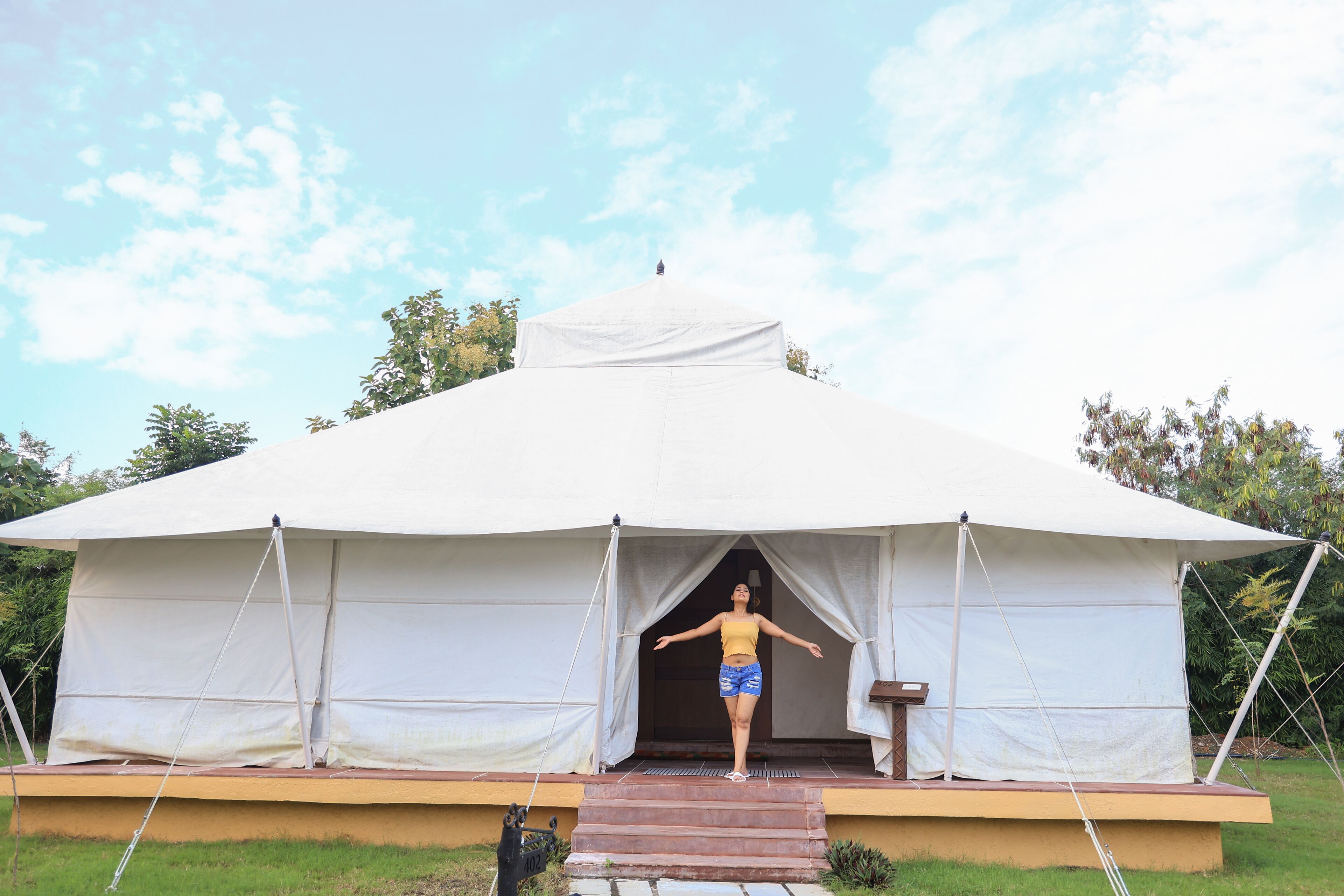 A large white tent with a flat roof, a wooden platform at the entrance, and a person standing in the doorway.