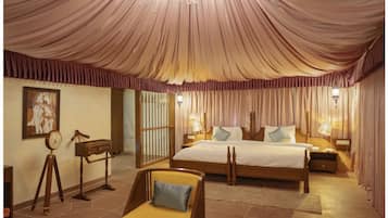 A spacious bedroom with a large bed, a sitting area with a chair, and a chandelier.