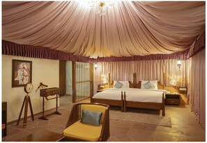 A spacious bedroom with a large bed, a sitting area with a chair, and a chandelier. - WelcomHeritage Tadoba Vanya Villas Resort & Spa (Chimur)