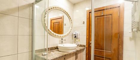 A bathroom with a glass shower enclosure, a wooden door, a marble countertop, and a white sink.