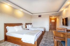 A hotel room with two beds, a desk, a chair, a TV, and a door leading to another room. - Helen Troya Hotel Geyikli (Ezine)