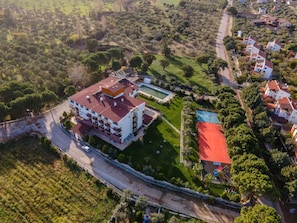 Vista aérea de una zona residencial con un edificio de varios pisos, una piscina y una cancha de tenis.