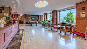 A hotel lobby with a reception desk, a pool table, seating area, and large windows. - Helen Troya Hotel Geyikli (Ezine)