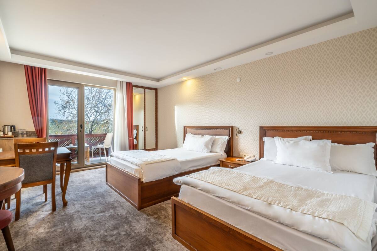 A hotel room with two beds, a desk, a chair, and a balcony with a view.