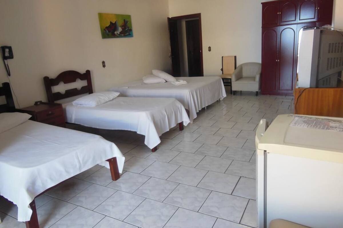 A hotel room with three single beds, a desk, a chair, a wardrobe, and a painting on the wall.