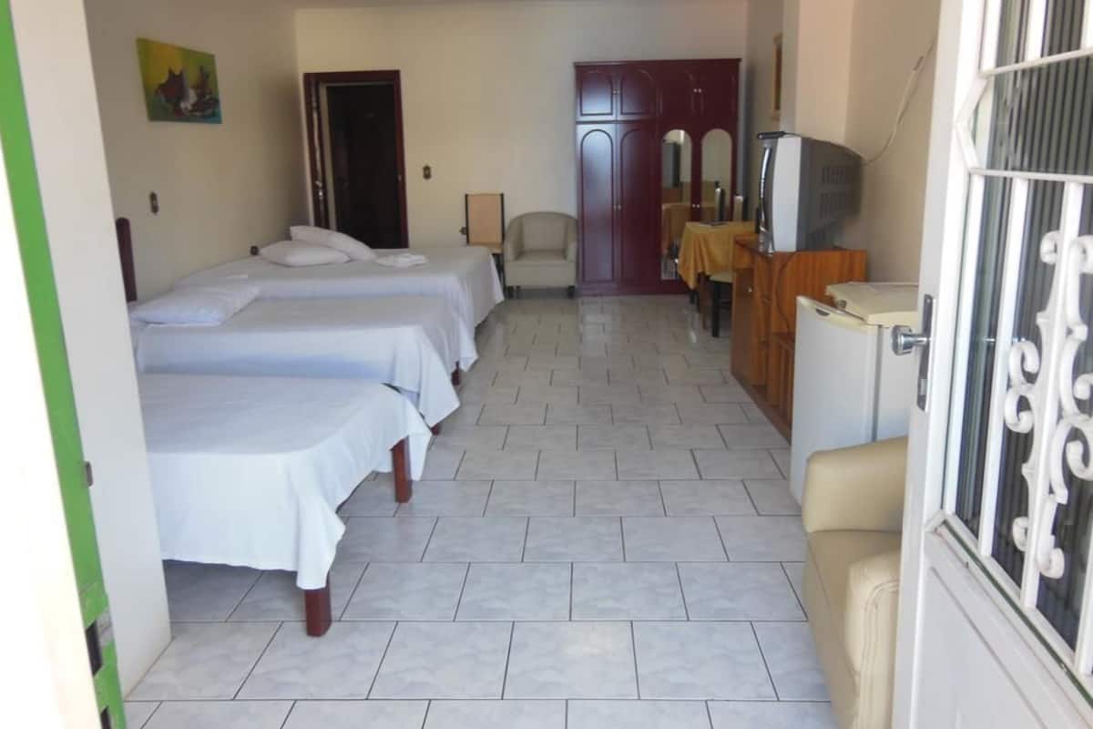 A hotel room with two beds, a desk with a television, a wardrobe, and a door leading to another room.