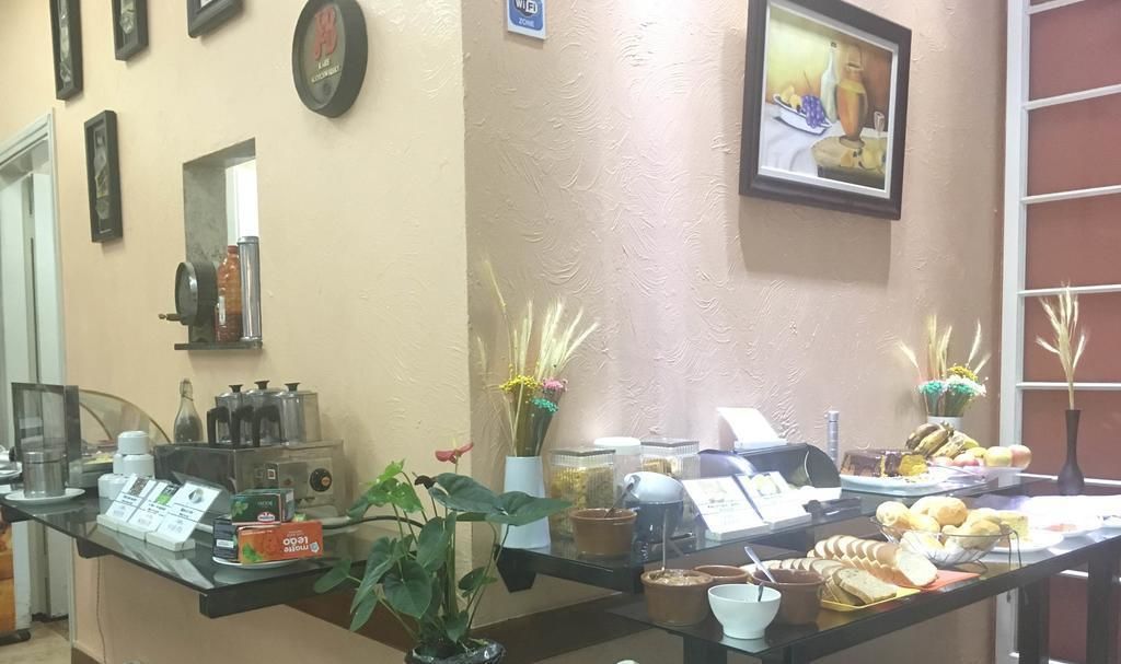 Espaço de buffet de café da manhã com diversas opções de alimentos, uma máquina de café e plantas decorativas.