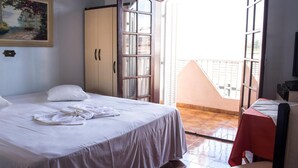 Una habitación de hotel con una cama, un armario, una mesa con mantel rojo y un balcón con vistas.