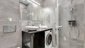 Ett modernt badrum med en inbyggd tvättmaskin, en duschkabin med glasväggar och en stor spegel.