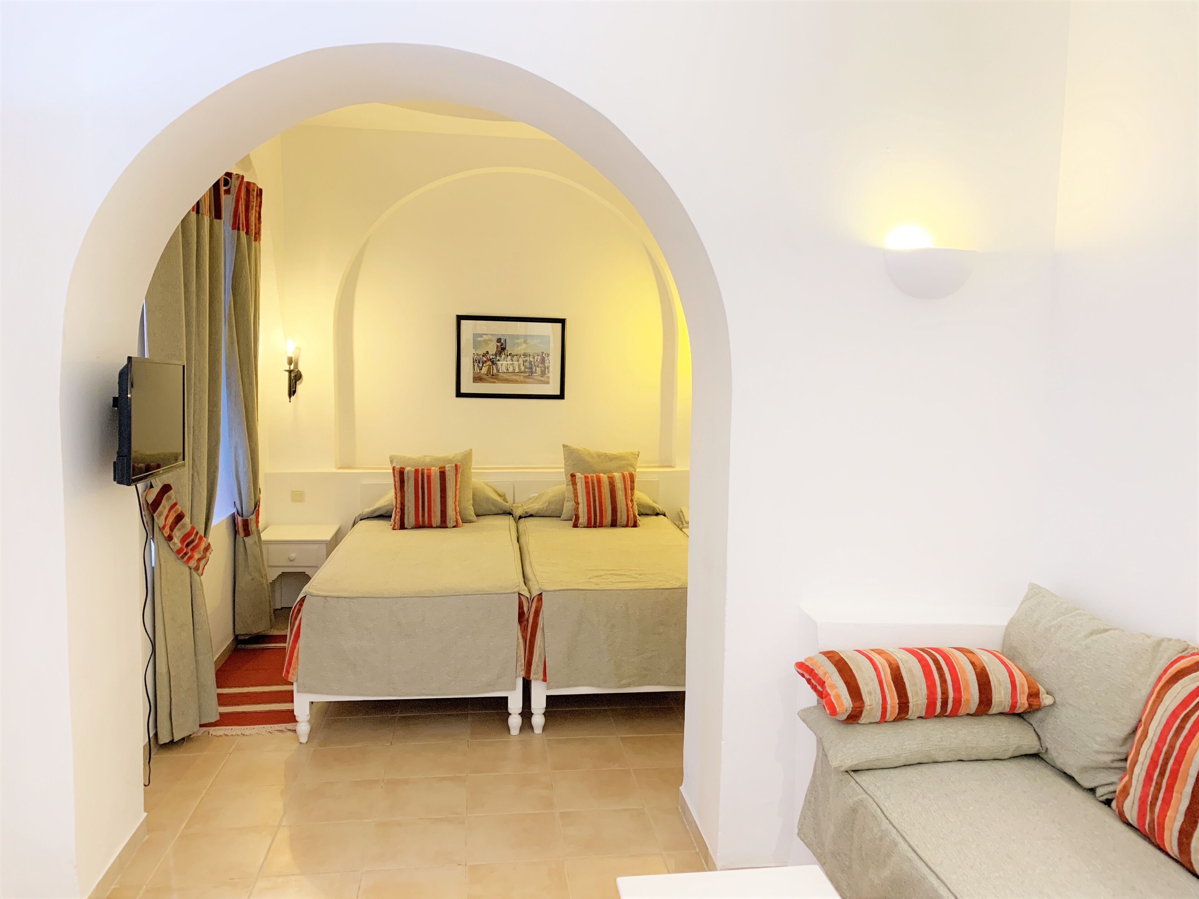 A hotel room with two beds, a sofa, a TV, and a framed picture on the wall.