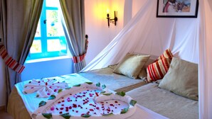 Een kamer met een bed, een raam met gordijnen, een wandlamp en een lijst met een afbeelding.
