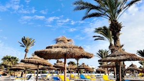 Een strand met rijen ligbedden en rieten parasols.