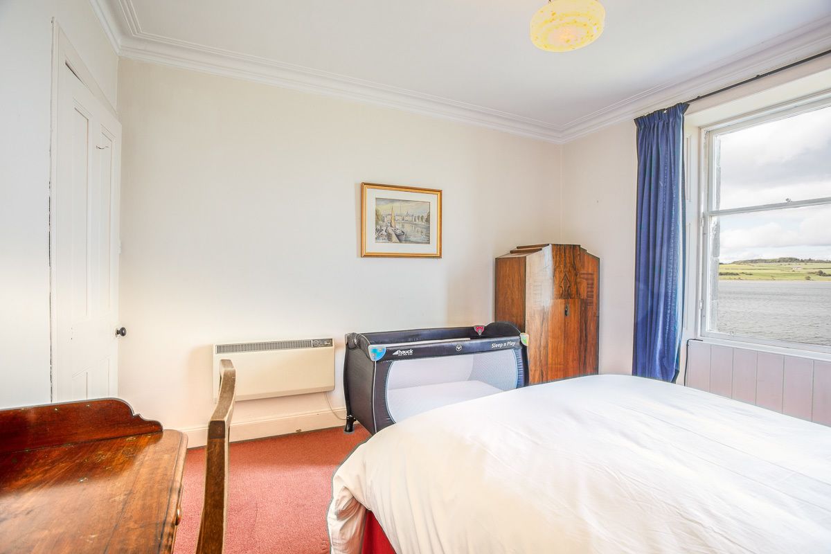 Quarto de hotel com uma cama, um banco de madeira, um radiador, um quadro na parede e vista para o mar pela janela.