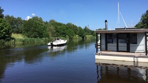 A calm river with a houseboat docked on the right, surrounded by lush greenery. - Hausboot Resort Nordseeküste (Wilhelmshaven)