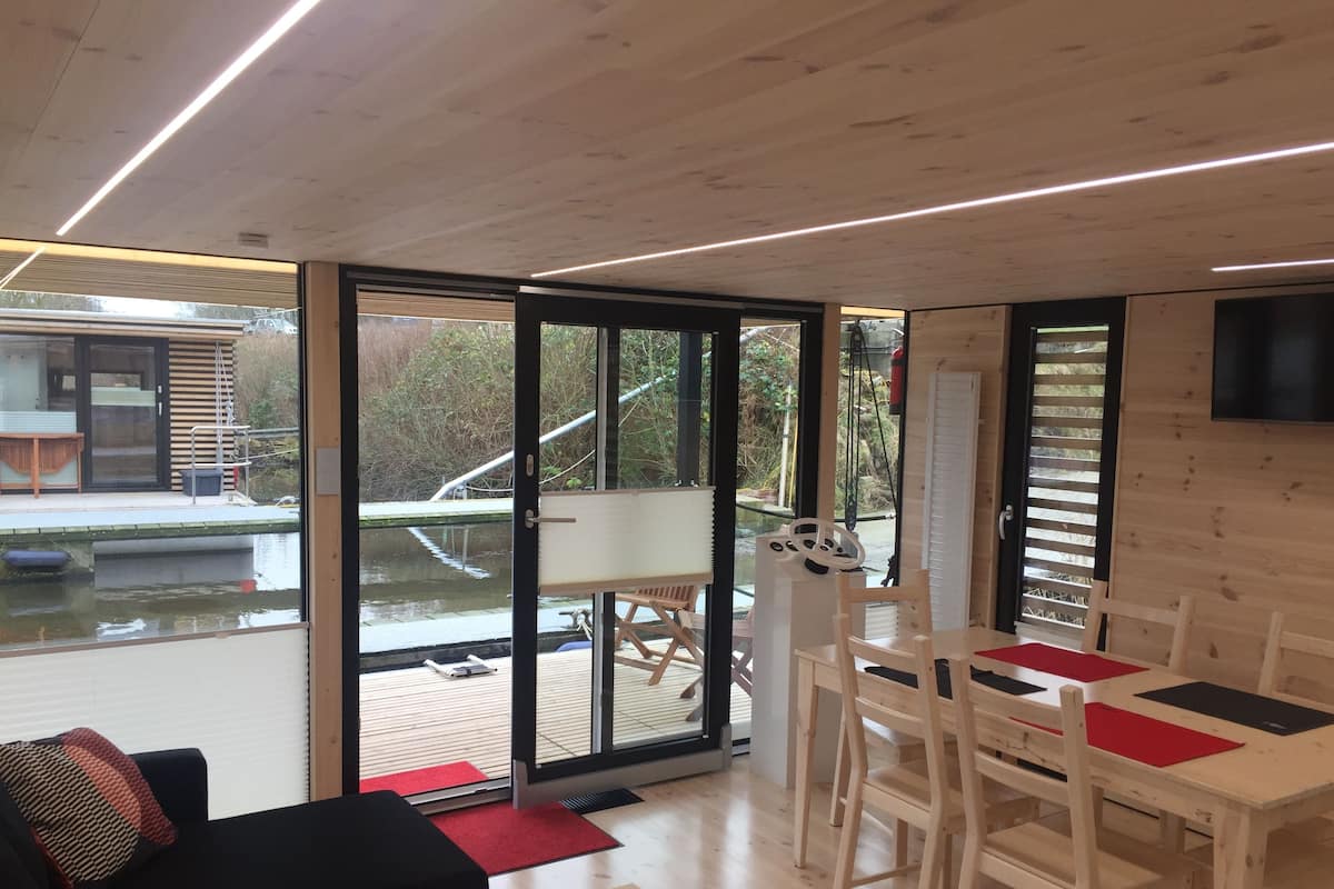 A modern interior with a dining area, a sofa, and a view of a water body outside.
