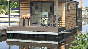 A floating house with a deck, a table, and chairs. - Hausboot Resort Nordseeküste (Wilhelmshaven)
