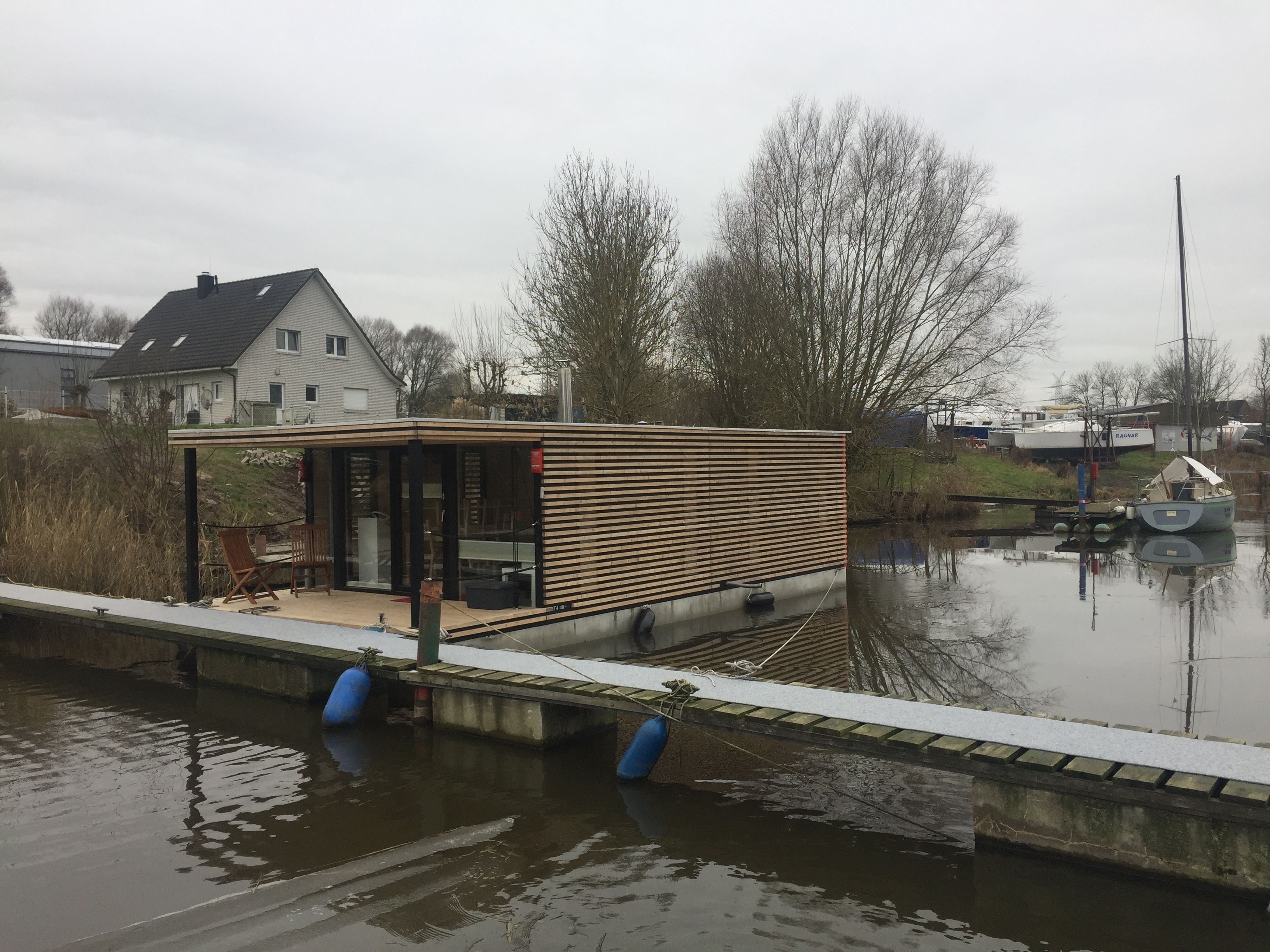 A modern, single-story house with a large deck area overlooking a calm body of water.