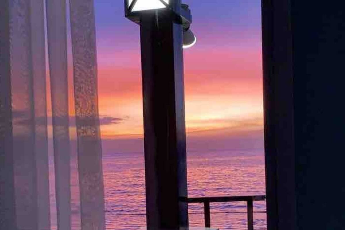 A room with a view of the sunset over the ocean, a window with a light fixture, and a brick wall.